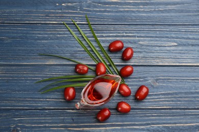 Photo of Palm oil in glass jug, tropical leaf and fruits on blue wooden table, flat lay