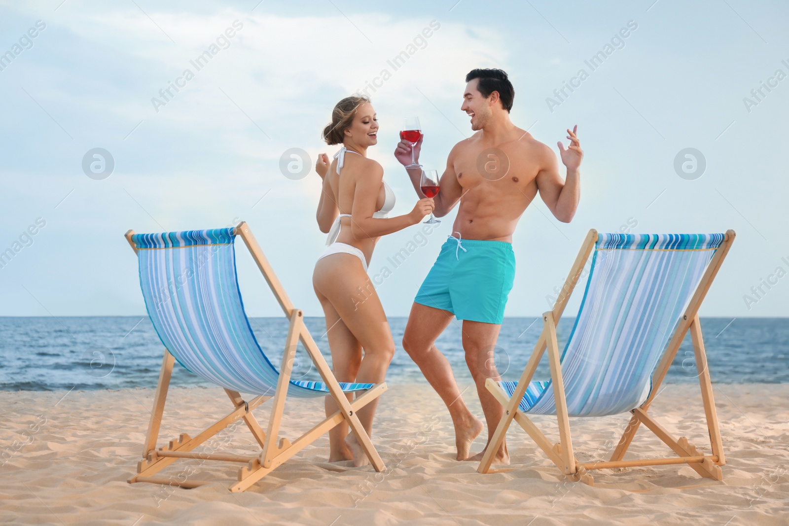 Photo of Happy young couple dancing near deck chairs at sea beach