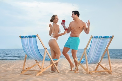 Photo of Happy young couple dancing near deck chairs at sea beach