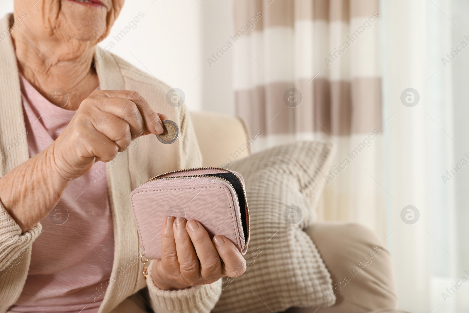 Photo of Elderly woman putting coin into wallet indoors, closeup. Space for text