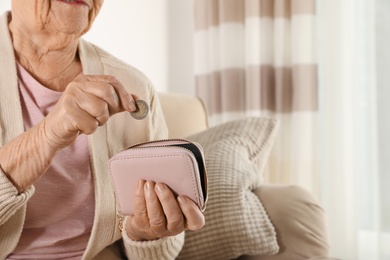 Elderly woman putting coin into wallet indoors, closeup. Space for text