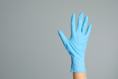 Doctor wearing medical gloves on grey background, closeup. Space for text