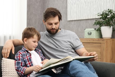 Dad and son reading book together on sofa at home