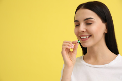 Photo of Young woman taking vitamin pill on yellow background. Space for text
