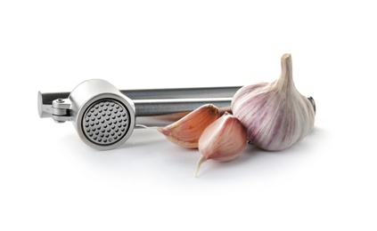 Photo of Garlic press and cloves on white background. Kitchen utensil