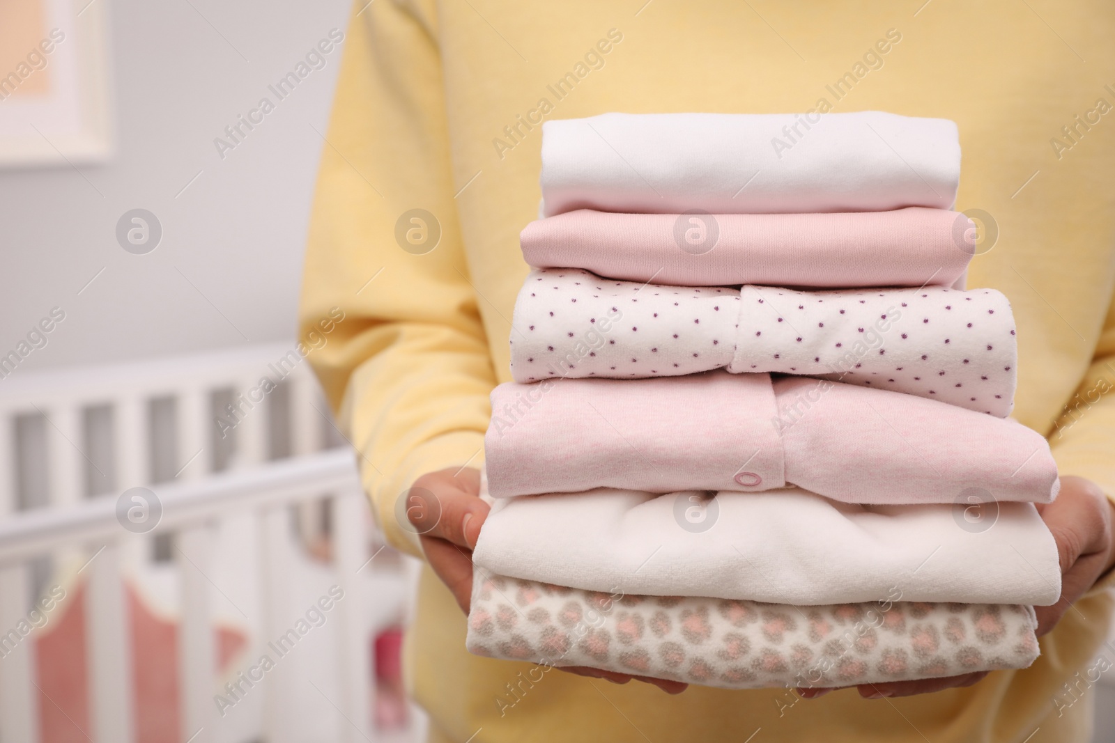 Photo of Woman holding stack of girl's clothes indoors, closeup