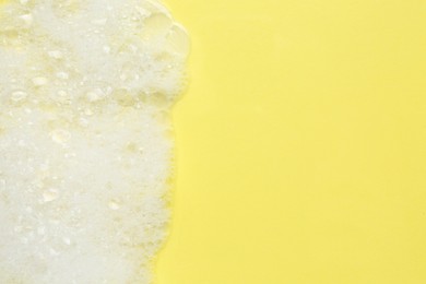 Photo of Fluffy bath foam on yellow background, top view. Space for text