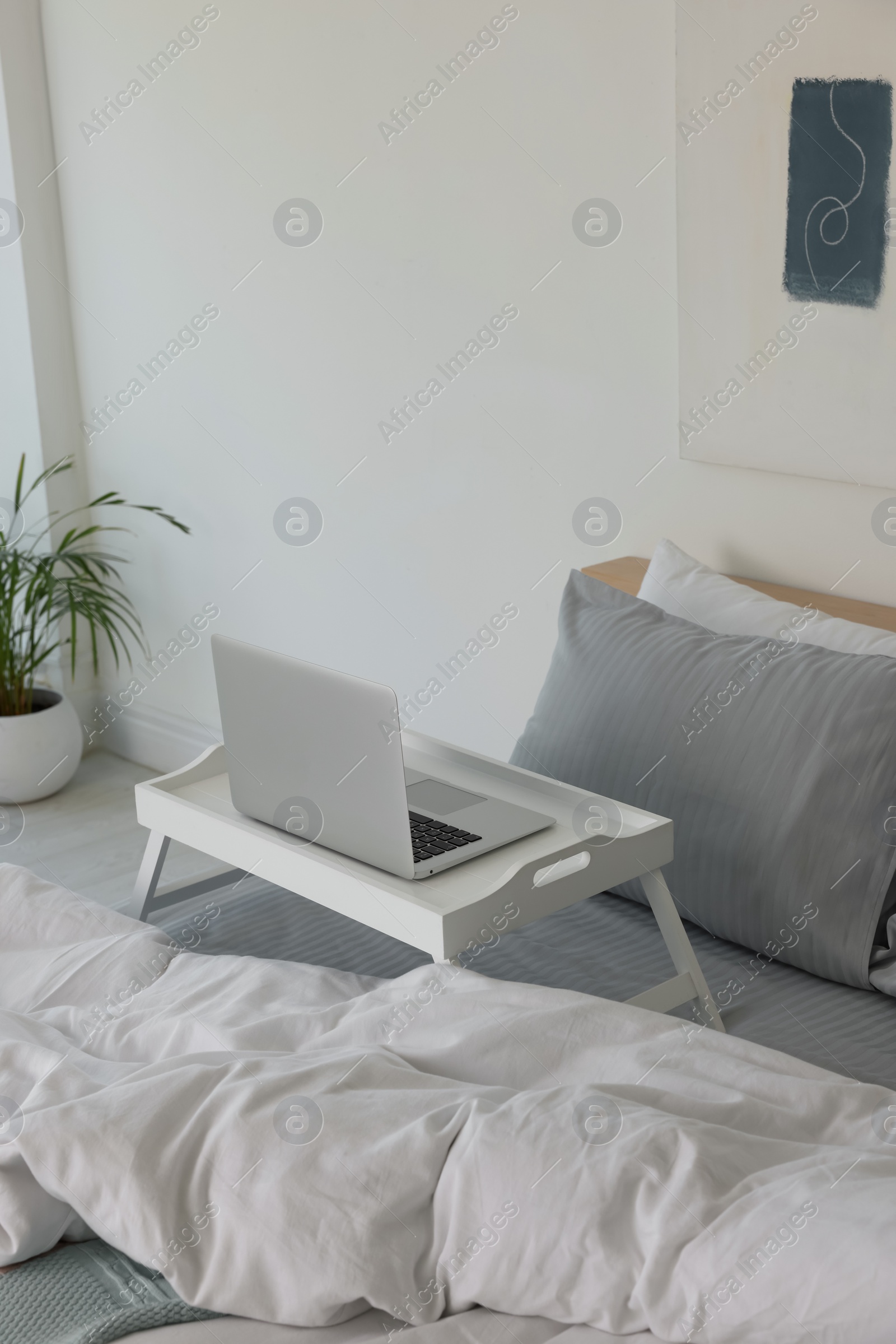 Photo of White tray table with laptop on bed indoors