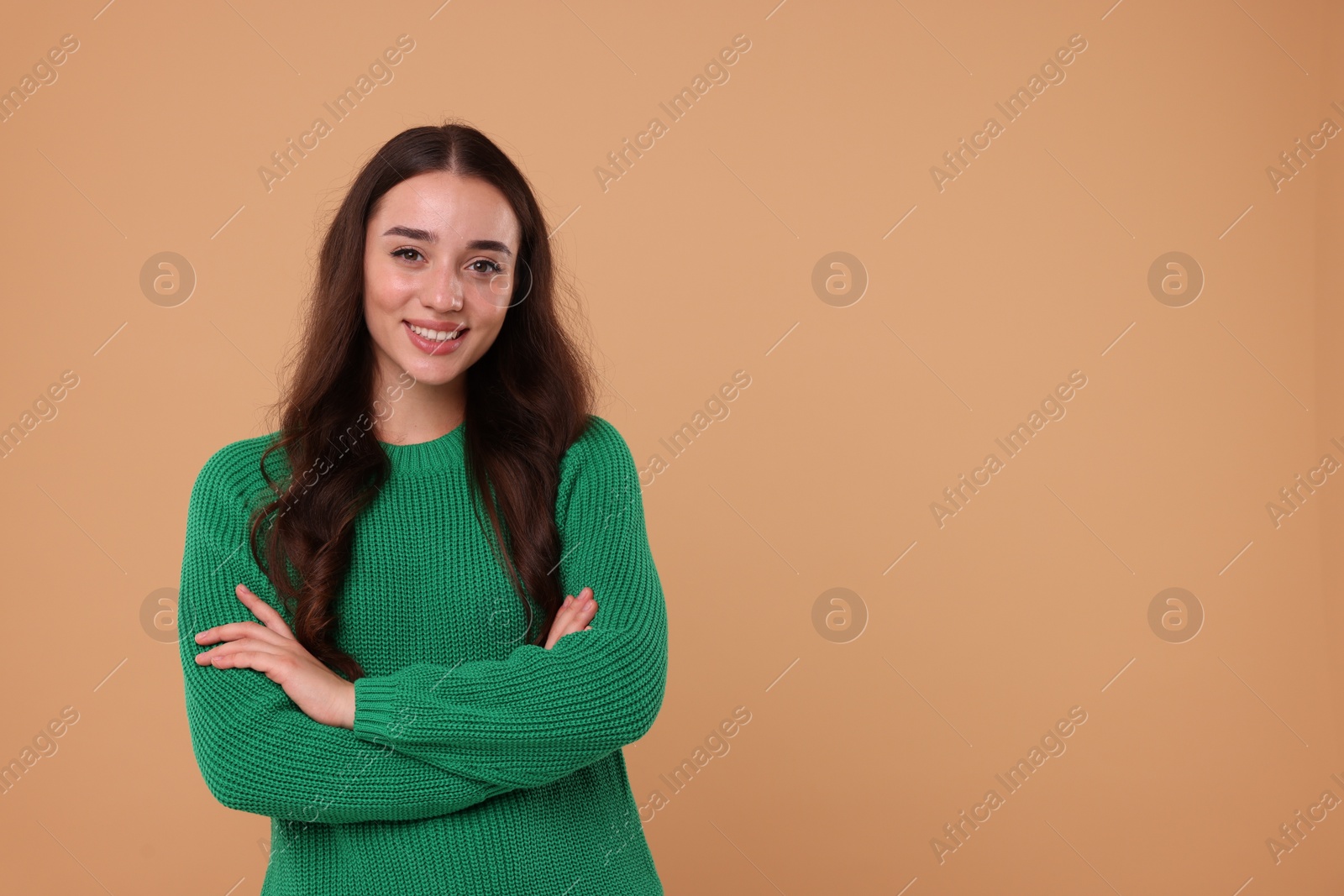 Photo of Beautiful young woman in stylish warm sweater on beige background, space for text