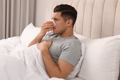 Photo of Sick man with tissue suffering from cold in bed at home