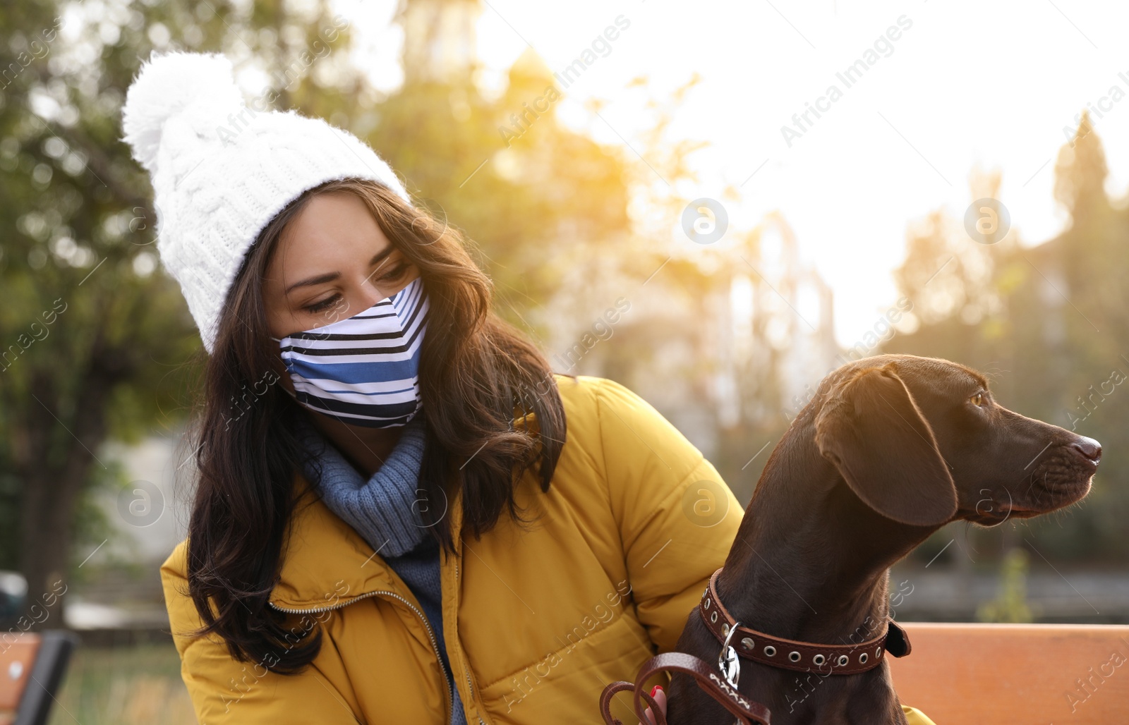 Photo of Woman in protective mask with German Shorthaired Pointer outdoors. Walking dog during COVID-19 pandemic