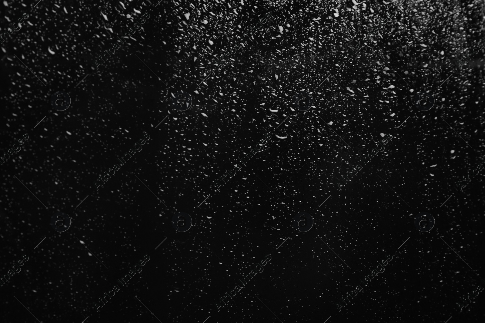 Photo of Glass with rain drops on black background