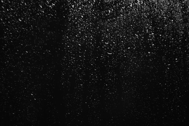 Photo of Glass with rain drops on black background