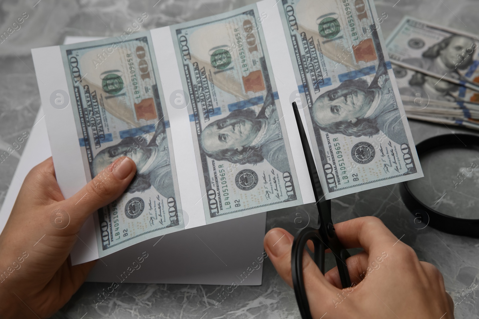 Photo of Counterfeiter cutting dollar banknotes with scissors at grey marble table, closeup. Fake money