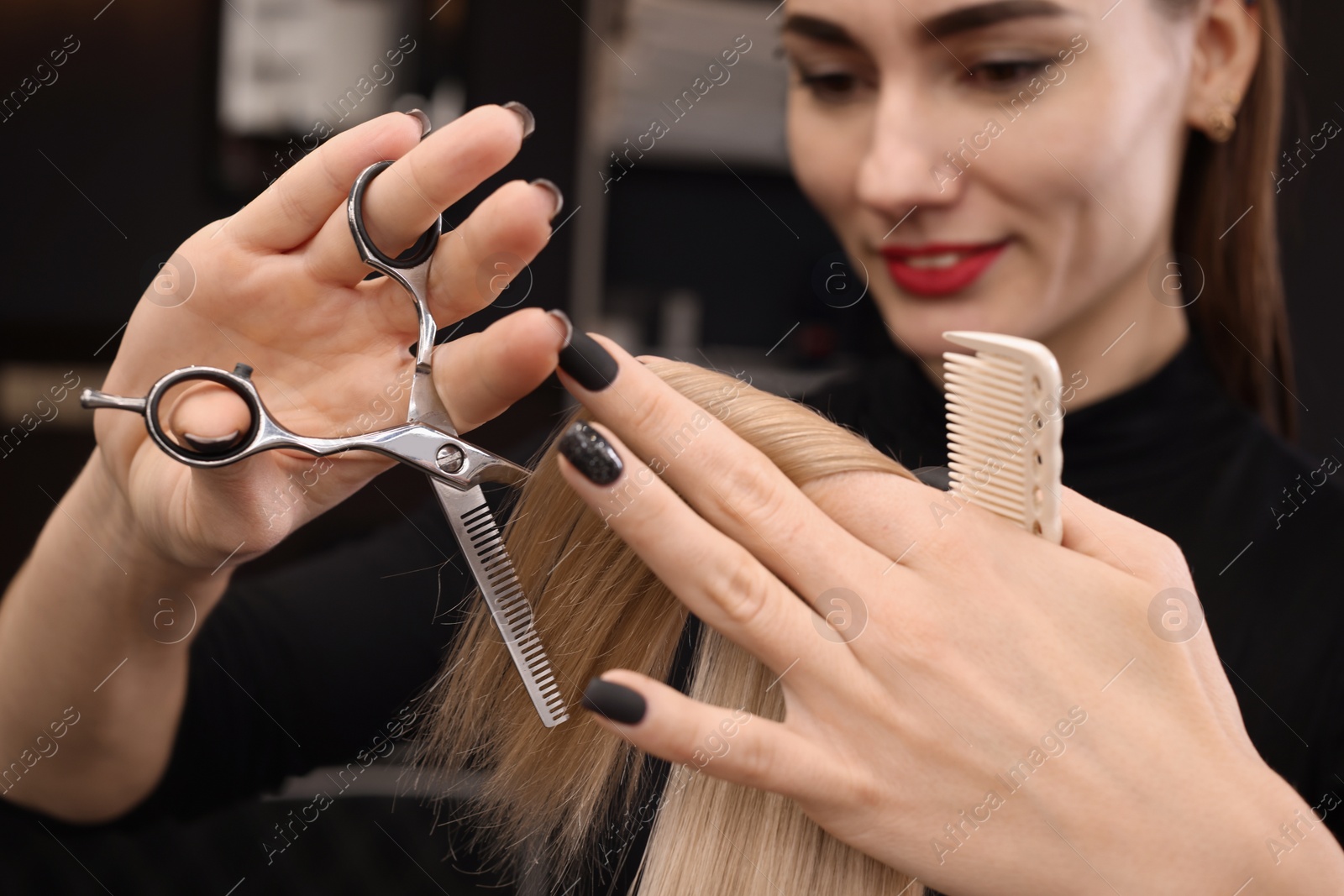 Photo of Professional hairdresser cutting woman's hair in salon, focus on hands