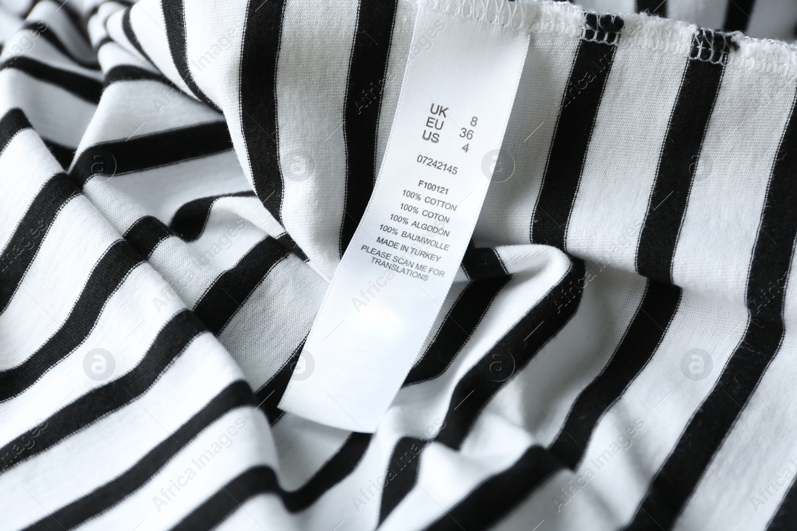 Photo of Clothing label with size and content information on striped garment, closeup