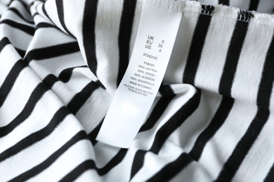 Photo of Clothing label with size and content information on striped garment, closeup