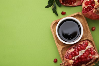 Photo of Flat lay composition with tasty pomegranate sauce and fruits on green table. Space for text