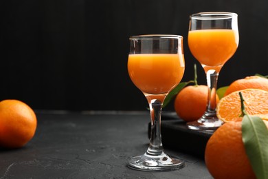 Photo of Tasty tangerine liqueur in glasses and fresh citrus fruits on black textured table. Space for text