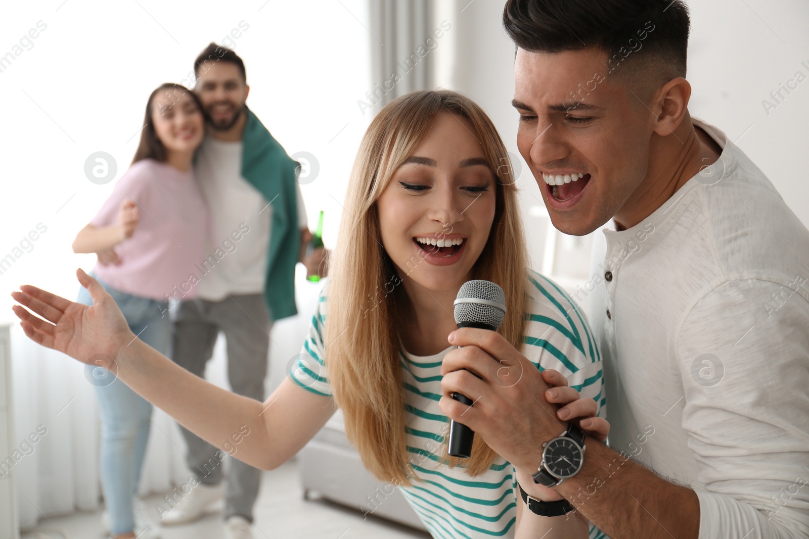 Photo of Happy couple singing karaoke with friends at home