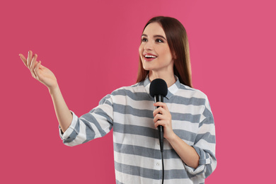 Photo of Young female journalist with microphone on pink background