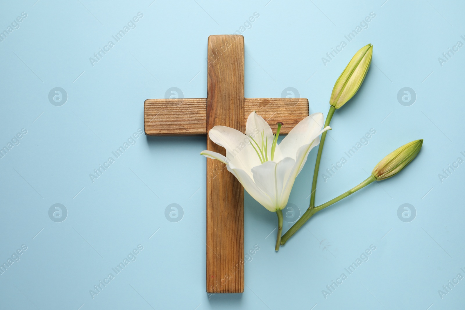 Photo of Wooden cross and lily flowers on light blue background, top view. Easter attributes