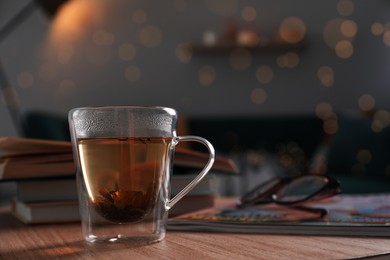 Glass cup of hot tea on wooden table in living room, space for text. Cozy home atmosphere