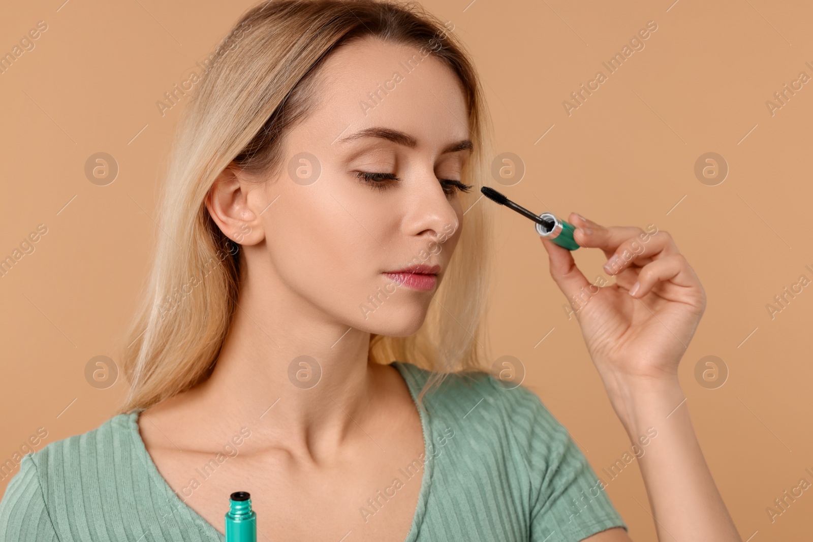 Photo of Beautiful woman applying mascara on beige background