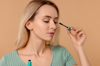 Photo of Beautiful woman applying mascara on beige background