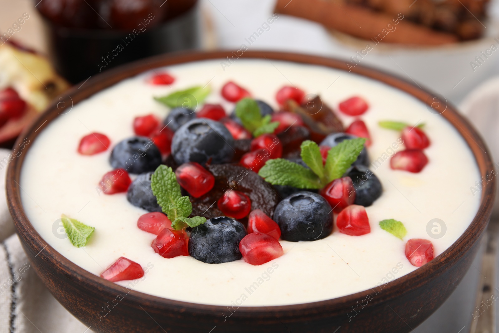 Photo of Delicious semolina pudding with blueberries, pomegranate, dates and mint in bowl on table, closeup