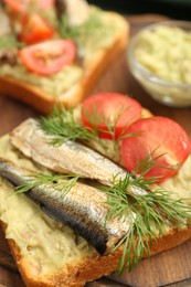 Photo of Delicious sandwich with sprats, tomato, dill and avocado puree on wooden table, closeup