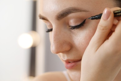 Photo of Makeup product. Woman applying black eyeliner indoors, closeup