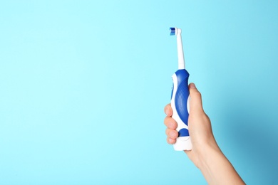 Woman holding electric toothbrush against color background