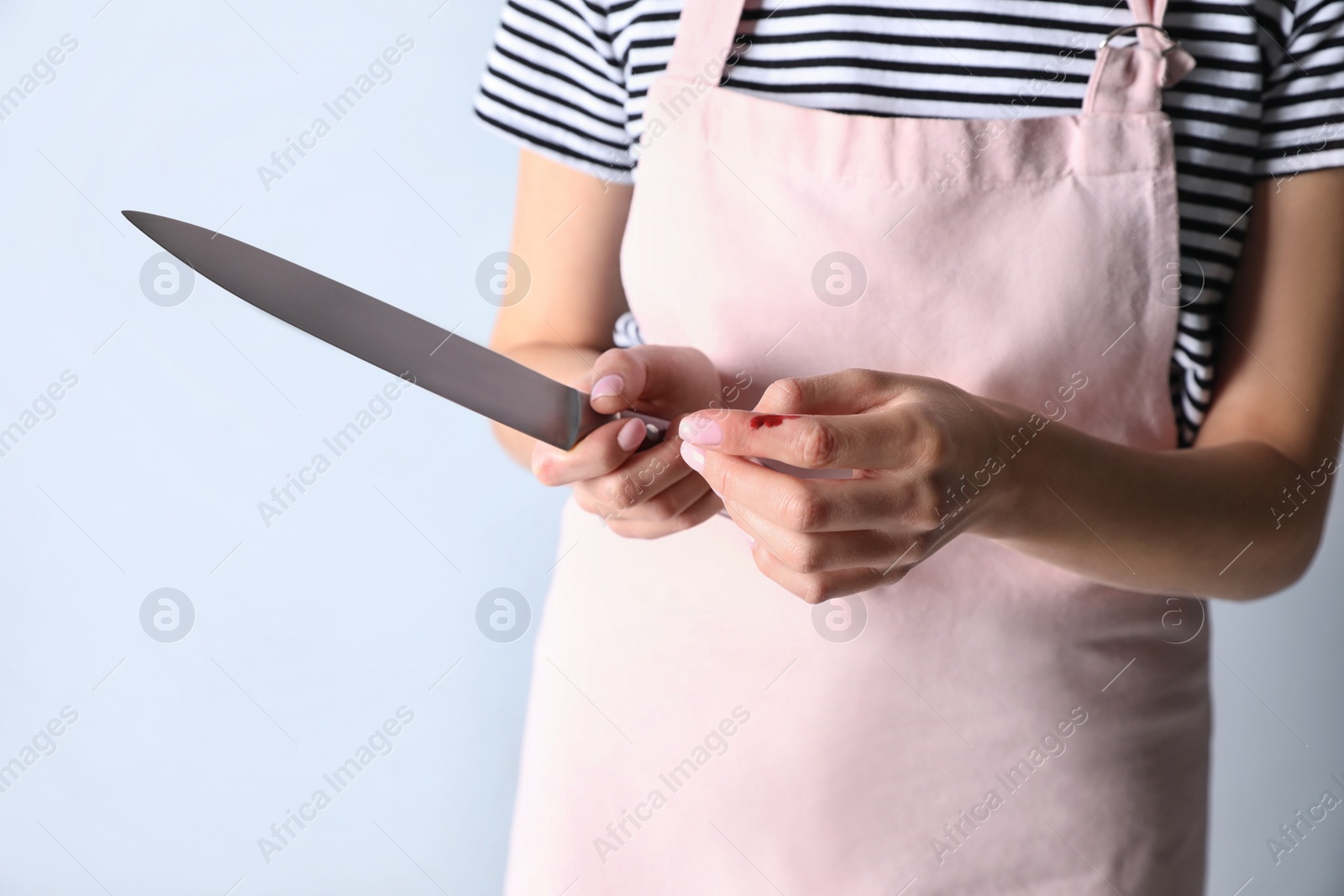 Photo of Woman cutting finger with knife on light grey background, closeup