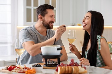 Photo of Affectionate couple enjoying cheese fondue during romantic date in kitchen