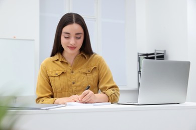Young female intern working with laptop at table in office