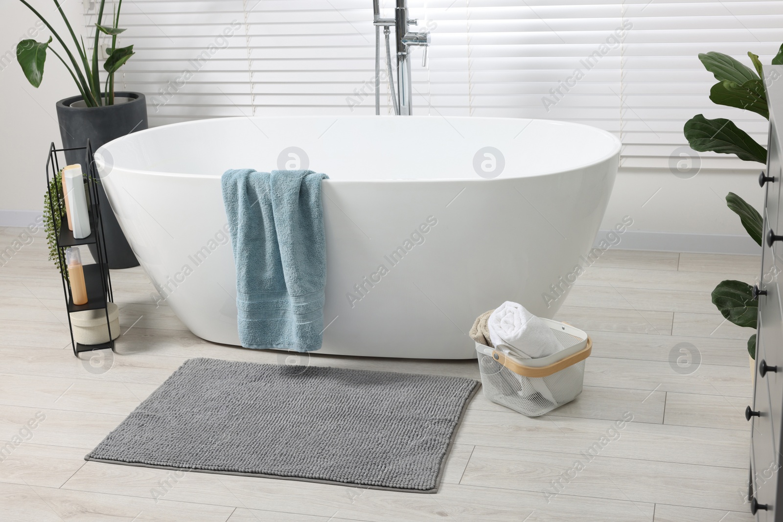 Photo of Stylish bathroom interior with bath tub, houseplants and soft light grey mat