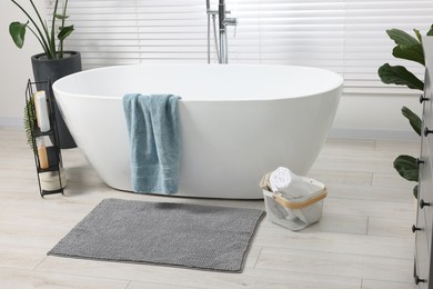 Stylish bathroom interior with bath tub, houseplants and soft light grey mat