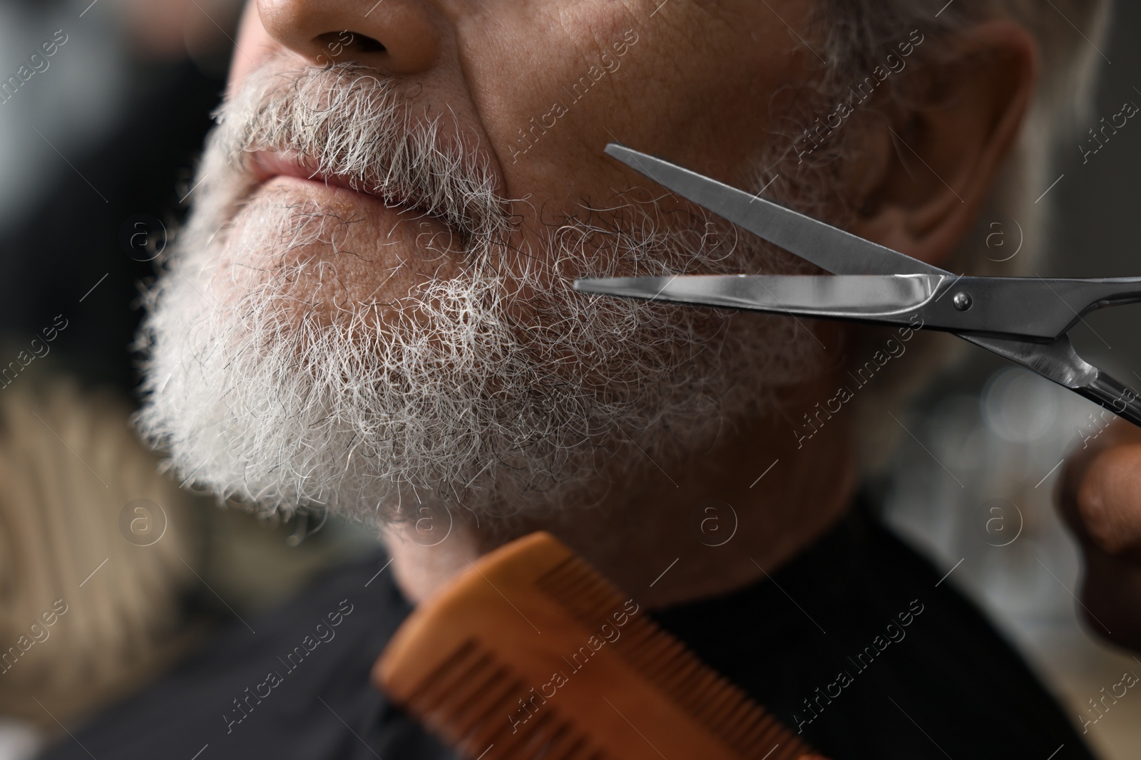 Photo of Professional barber trimming client's beard with scissors in barbershop, closeup