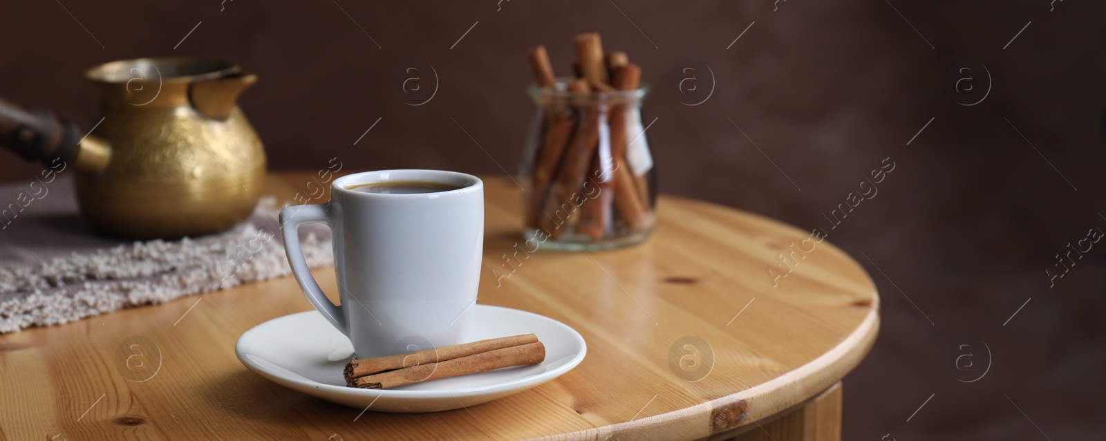 Image of Turkish coffee. Cup of freshly brewed beverage, cinnamon and cezve on wooden table. Banner design with space for text