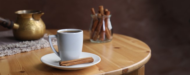 Image of Turkish coffee. Cup of freshly brewed beverage, cinnamon and cezve on wooden table. Banner design with space for text