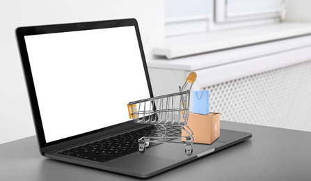 Image of Online shopping. Modern laptop with small cart and bags on table