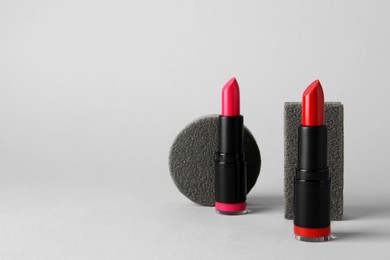 Photo of Beautiful red and pink lipsticks on light gray background, space for text