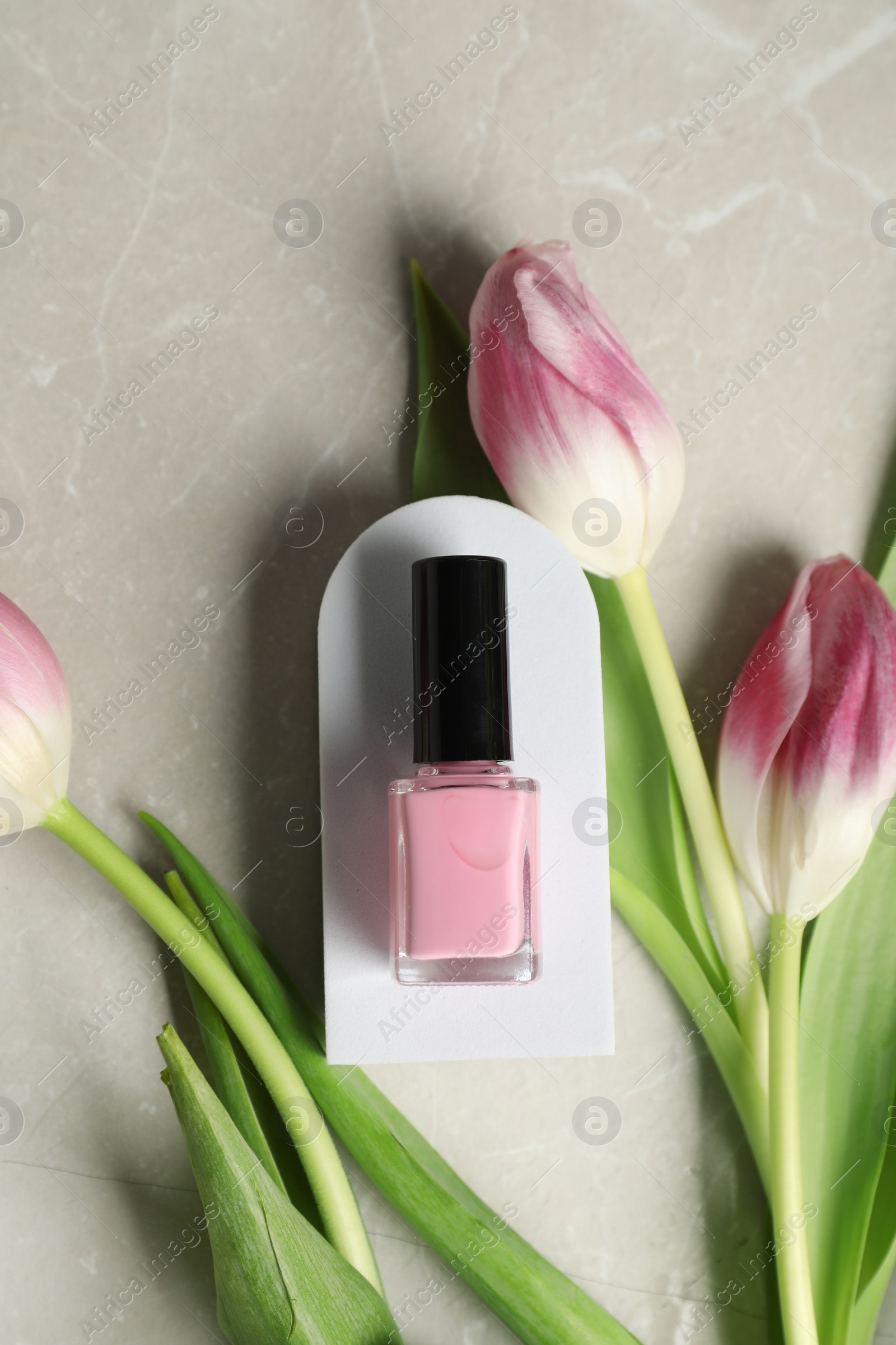 Photo of Flat lay composition with bright nail polish in bottle and tulip flowers on light textured table