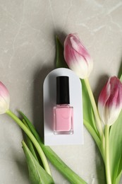 Flat lay composition with bright nail polish in bottle and tulip flowers on light textured table