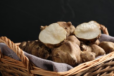 Wicker basket with many Jerusalem artichokes against dark background, closeup