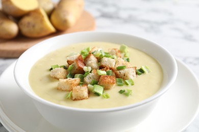 Tasty potato soup with croutons and green onion in bowl on white table, closeup