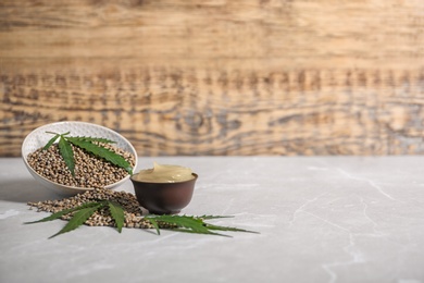 Photo of Bowl of hemp lotion and seeds on gray table with space for text against wooden background