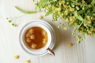 Photo of Cup of aromatic tea with linden blossoms on white wooden table, flat lay