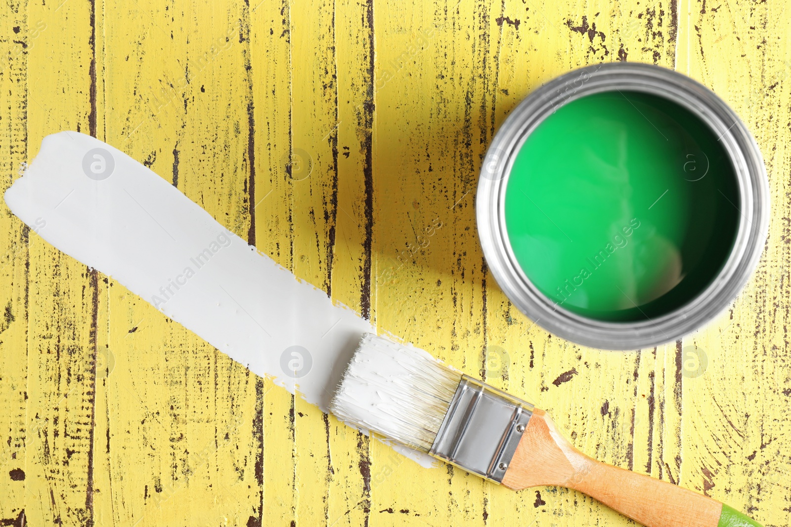 Photo of Open can, brush and paint stroke on yellow wooden table, flat lay. Space for text